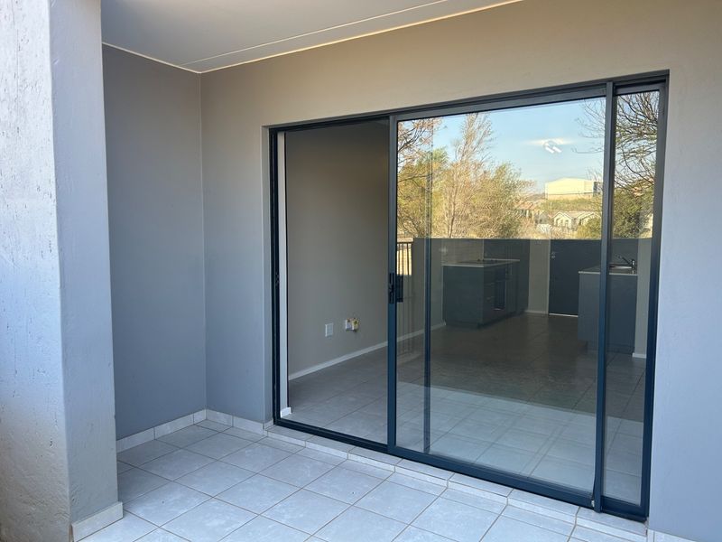 A clean, covered balcony area featuring tiled flooring and a large sliding glass door providing access to the interior living space.