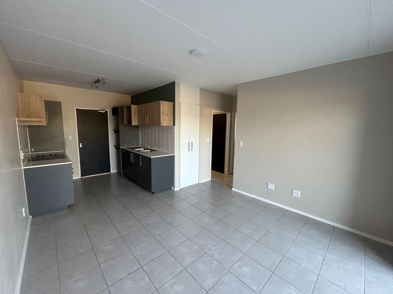 An open-plan living and kitchen area featuring tiled flooring, modern grey and wood-tone cabinetry, and a built-in cupboard for additional storage.