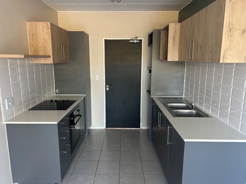Modern galley-style kitchen featuring grey and wood-tone cabinetry, quartz countertops, subway tile backsplash, and integrated electric hob and oven.