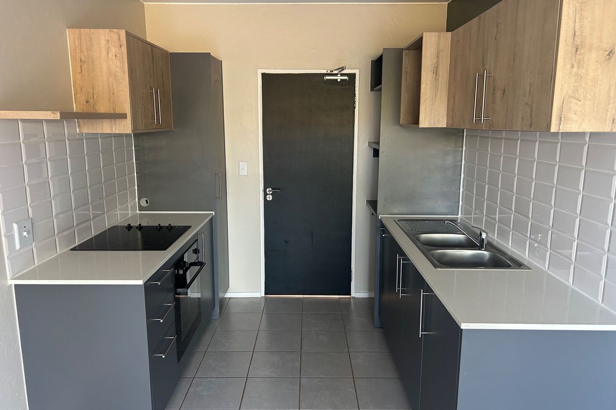 Modern galley-style kitchen featuring grey and wood-tone cabinetry, quartz countertops, subway tile backsplash, and integrated electric hob and oven.