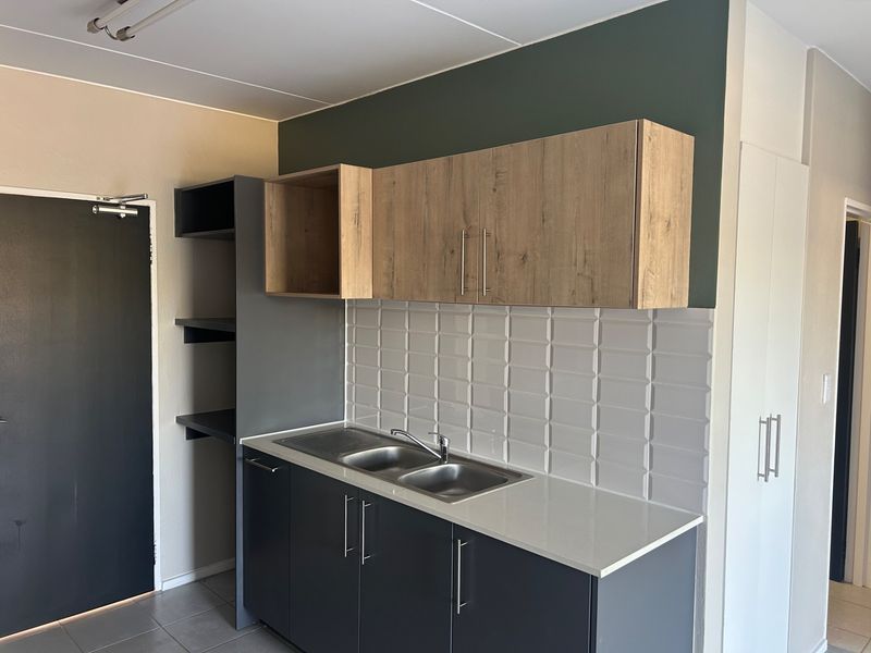 A modern, compact kitchen featuring dark grey base cabinets, wood-tone upper cabinets, a stone countertop, and a clean subway tile backsplash.