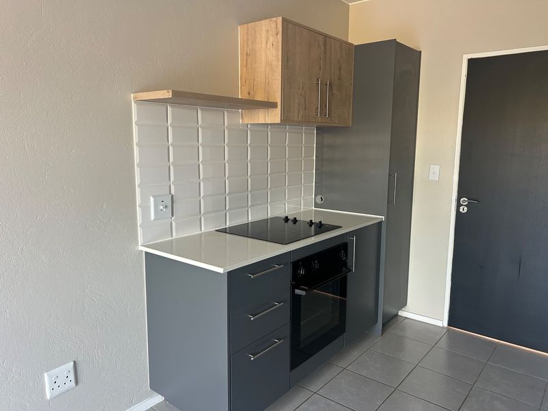 A modern, compact kitchen featuring grey cabinetry, a built-in oven and hob, subway tile backsplash, and stone countertops.