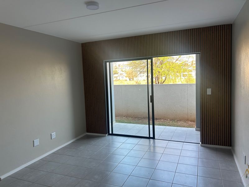 Modern living area featuring contemporary slatted wood wall paneling, neutral tiled flooring, and a sliding glass door providing direct access to a private patio.
