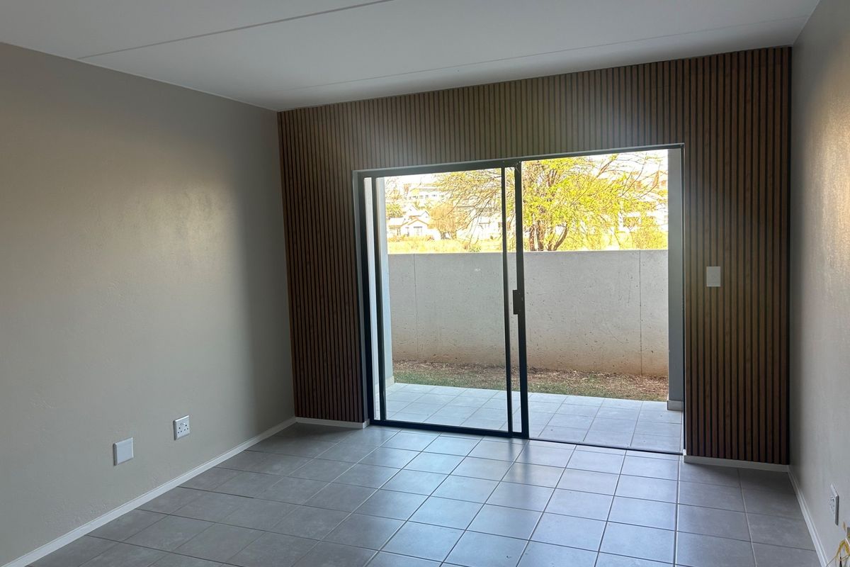Modern living area featuring contemporary slatted wood wall paneling, neutral tiled flooring, and a sliding glass door providing direct access to a private patio.