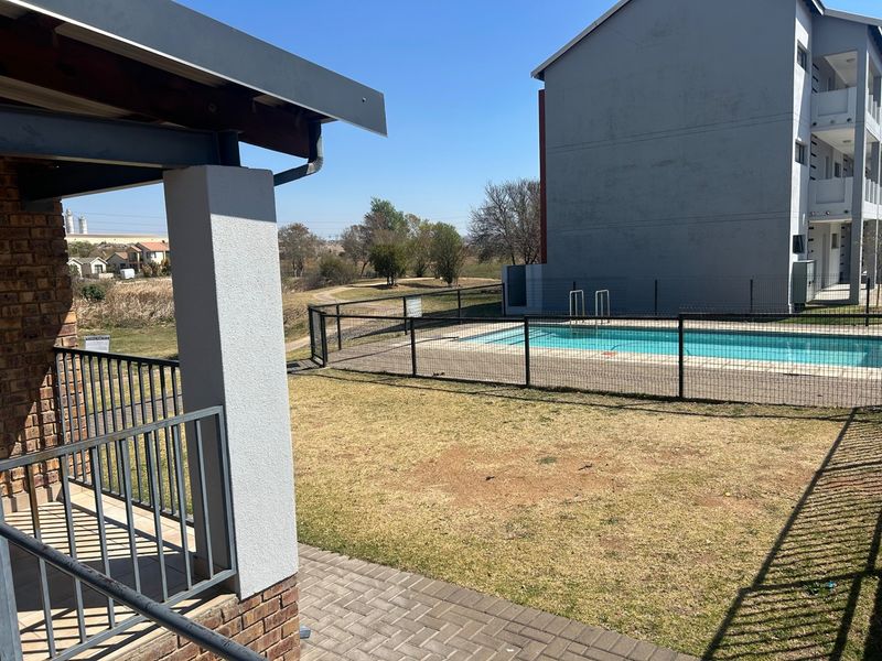 Outdoor view featuring a swimming pool with metal fencing, a paved patio area, and a covered balcony overlooking the communal grounds.