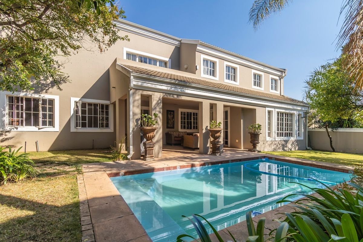 Rear view of the property featuring a covered patio area overlooking a private swimming pool with paved surround and landscaped garden.