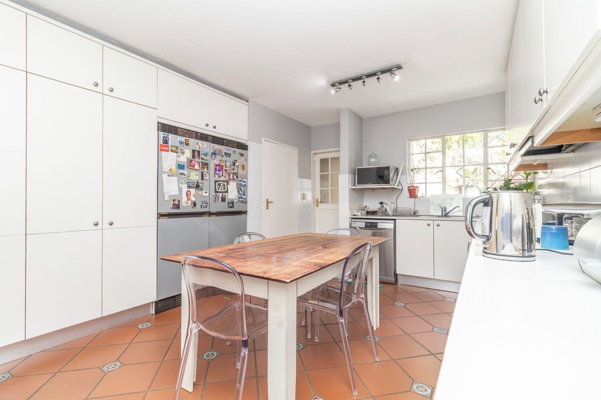 A functional kitchen featuring white cabinetry, tiled flooring, a double sink, and a dedicated dining area with ample storage space.