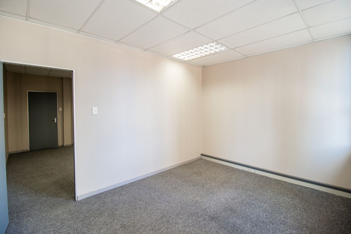 A clean, empty commercial office space featuring neutral walls, grey carpeting, and a suspended ceiling with recessed lighting.