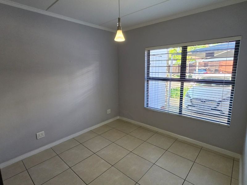 A clean, empty bedroom featuring neutral tiled flooring, a pendant light fixture, and window blinds, offering a versatile space ready for personalization.