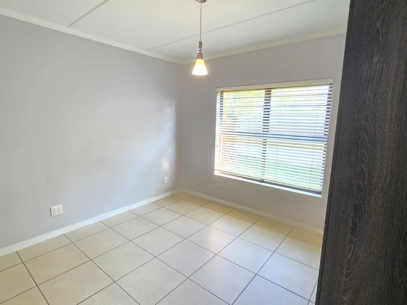 A clean, empty bedroom featuring neutral tiled flooring, a built-in cupboard, and a window fitted with venetian blinds.