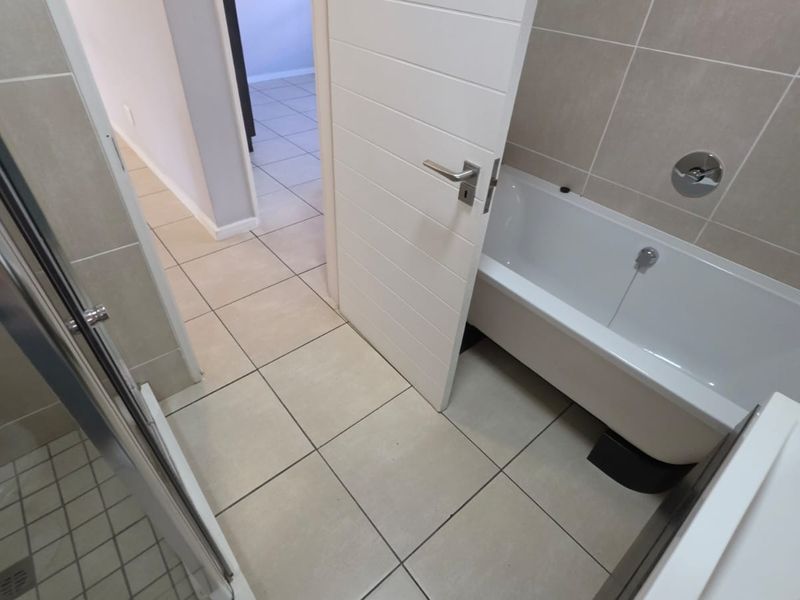 A clean, modern bathroom featuring a bathtub, separate shower enclosure, and neutral wall and floor tiling.