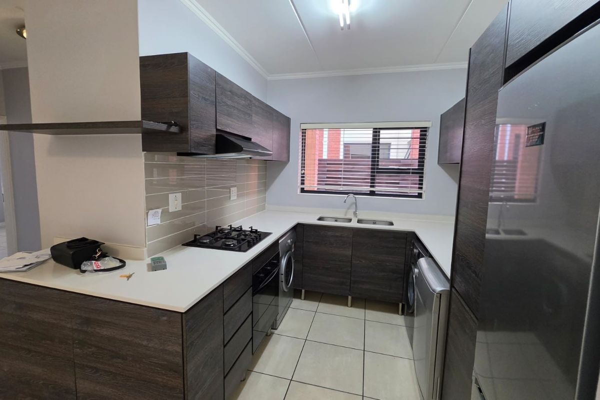 Modern kitchen featuring dark wood-grain cabinetry, stone-look countertops, a gas hob, extractor fan, and tiled flooring with a functional layout.