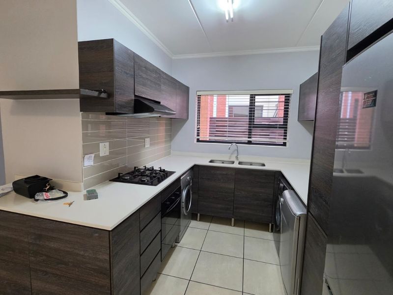 Modern kitchen featuring dark wood-grain cabinetry, stone-look countertops, a gas hob, extractor fan, and tiled flooring with a functional layout.