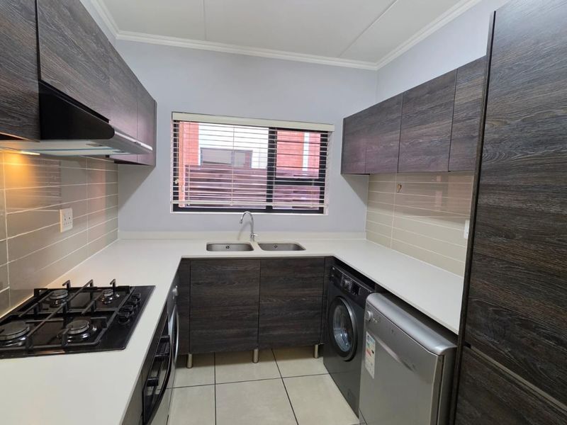 Modern kitchen featuring dark wood-grain cabinetry, stone countertops, gas hob, extractor fan, and integrated space for laundry appliances.