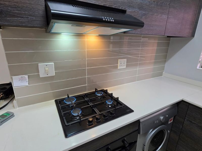 Modern kitchen featuring dark wood cabinetry, stone countertops, a gas hob with extractor fan, and an integrated washing machine.