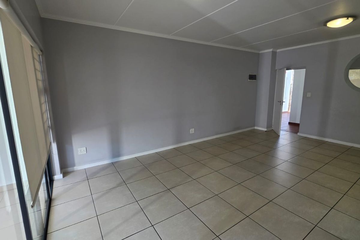 A spacious, empty living room featuring neutral grey walls, large format floor tiles, and a unique circular window, offering a bright and versatile living space.