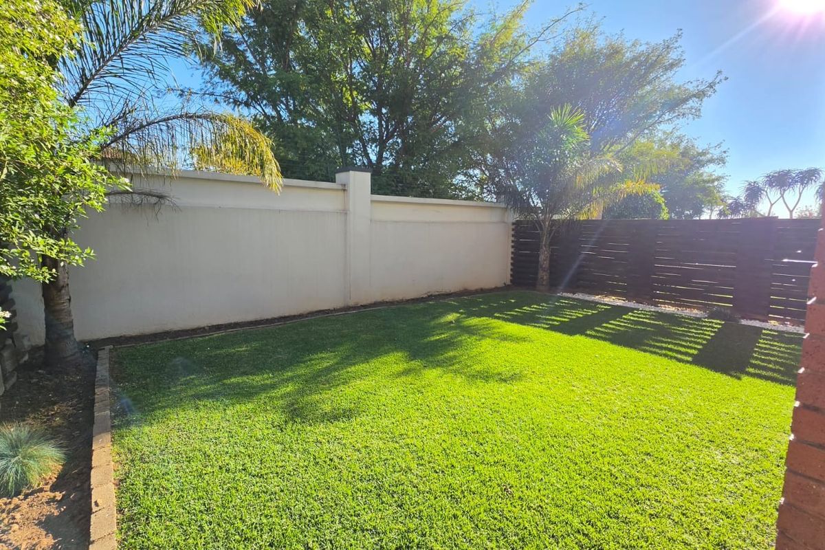A well-maintained private rear garden featuring a lush green lawn, perimeter boundary walls, and timber slat fencing.