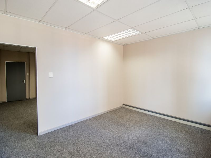 A clean, empty commercial office space featuring neutral walls, grey carpeting, and a suspended ceiling with recessed lighting.
