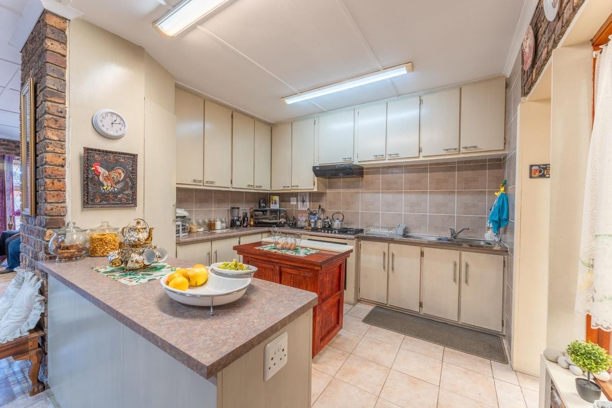 Functional kitchen featuring ample built-in cabinetry, tiled backsplash, stainless steel sink, and an exposed brick feature wall, offering a practical layout for daily use.