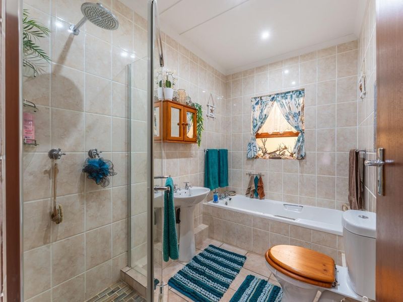 A functional bathroom featuring a pedestal basin, built-in bathtub, and a separate glass-enclosed shower with rainfall shower head, finished with neutral ceramic tiling.