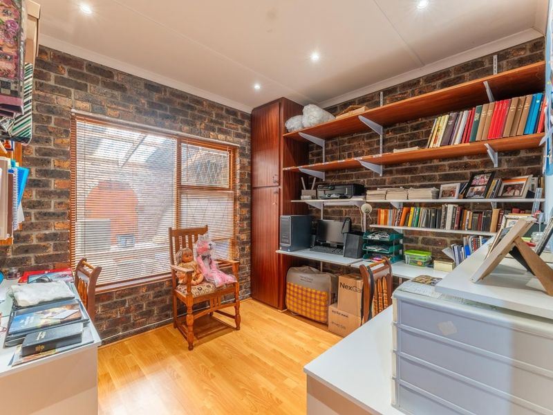 A functional home office featuring exposed brick walls, laminate flooring, and extensive built-in shelving for storage and workspace organization.