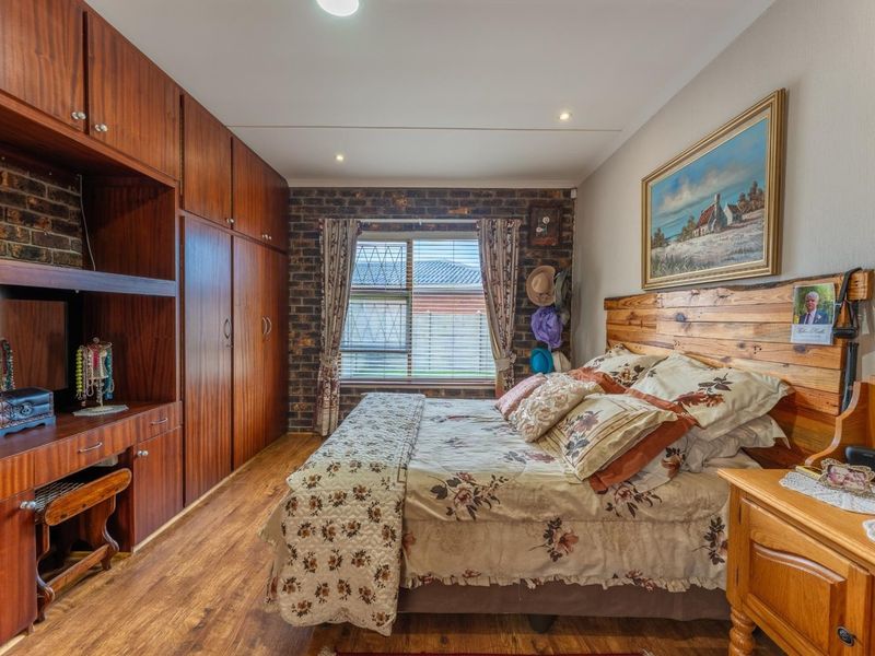 A cozy bedroom featuring warm wood-toned built-in cabinetry, an exposed brick feature wall, and durable laminate flooring with recessed lighting.