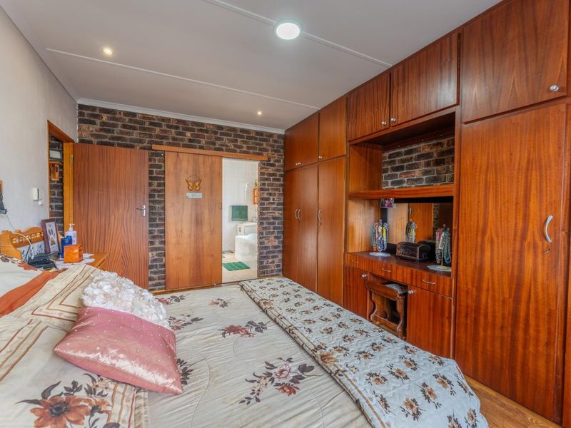 A bedroom featuring extensive built-in wooden cabinetry, an exposed brick feature wall, and direct access to an en-suite bathroom.