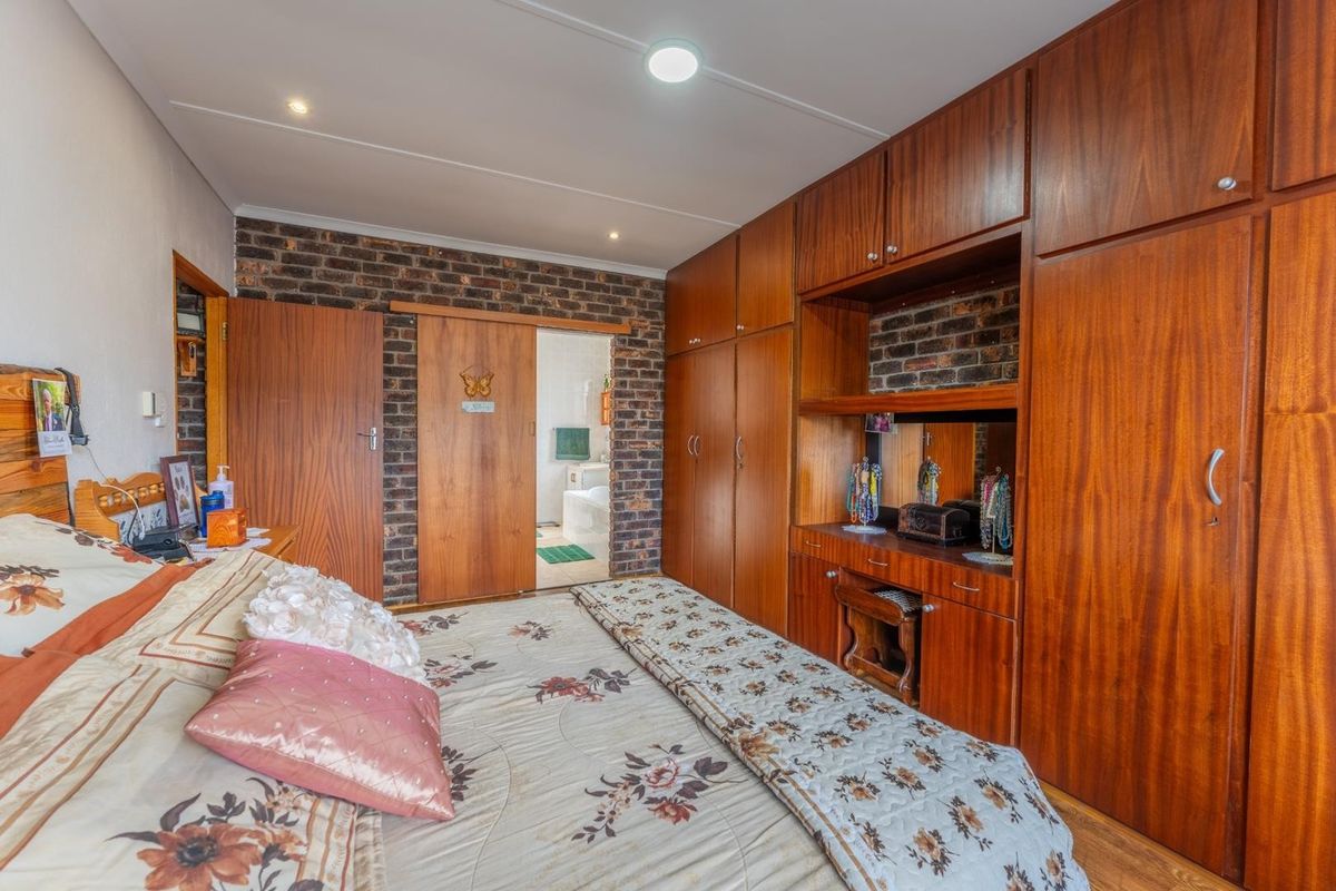 A bedroom featuring extensive built-in wooden cabinetry, an exposed brick feature wall, and direct access to an en-suite bathroom.