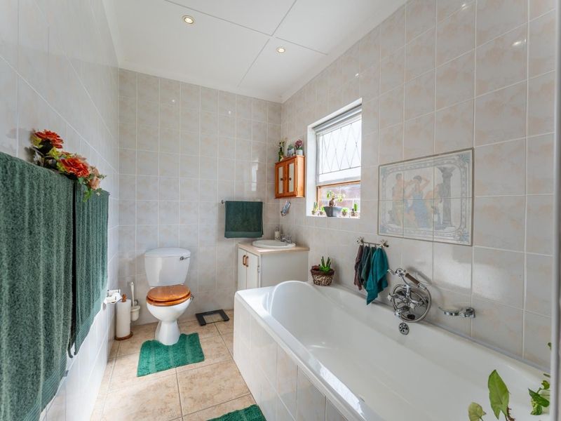 A functional bathroom featuring a bathtub, toilet, and vanity basin with neutral wall and floor tiling.