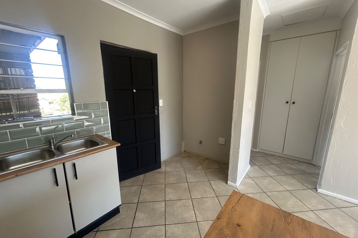 A clean, functional kitchen area featuring a double stainless steel sink, subway tile backsplash, and built-in storage cupboards with tiled flooring throughout.