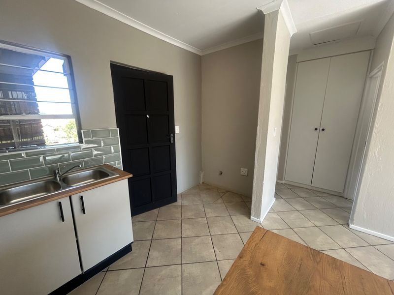 A clean, functional kitchen area featuring a double stainless steel sink, subway tile backsplash, and built-in storage cupboards with tiled flooring throughout.