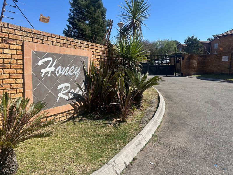 Entrance view of Honey Rock complex featuring a brick boundary wall, electric fencing, and secure gated access point.
