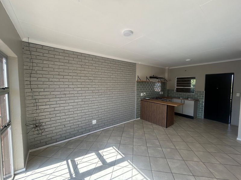 Open plan living and kitchen area featuring a grey brick feature wall, tiled floors, and a functional kitchen with a breakfast bar.