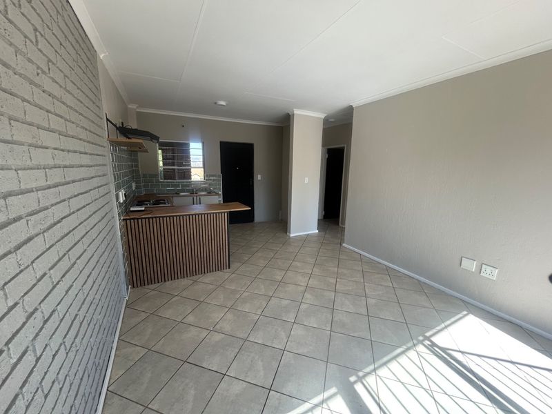Open-plan living area featuring tiled flooring, a brick feature wall, and a compact kitchen with a breakfast bar and modern finishes.