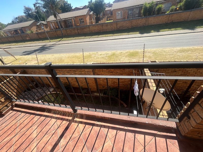 An elevated balcony featuring tiled flooring and a metal balustrade, overlooking a private garden area and the street.