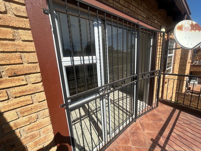 A balcony area featuring tiled flooring, a brick exterior facade, and a secure metal gate over the sliding door entrance.