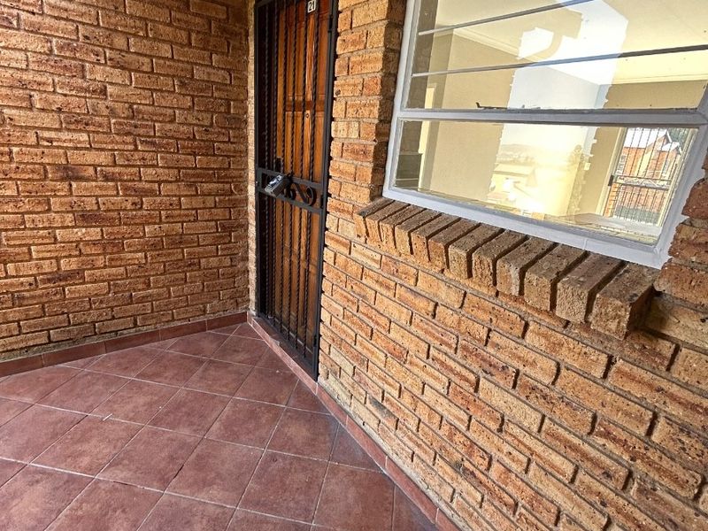 Entrance area featuring face brick walls, tiled flooring, and a secure metal gate, providing a functional and durable entry point to the apartment.