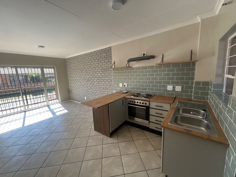 Modern open-plan kitchen and living area featuring a built-in oven, hob, subway tile backsplash, and an exposed brick feature wall with access to a balcony.