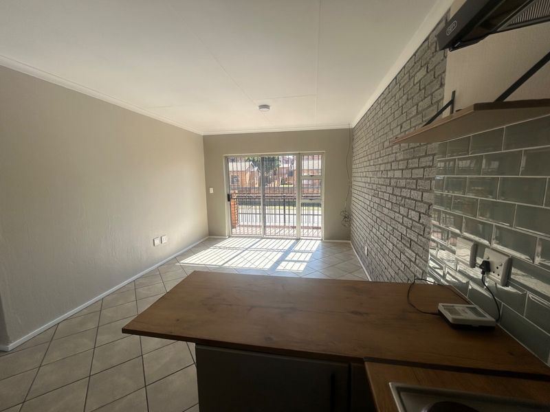 Open-plan living area featuring a brick accent wall, subway tile backsplash, wooden breakfast bar, and sliding door access to a balcony.