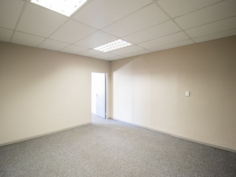 A clean, empty office space featuring neutral walls, grey carpeting, and a suspended ceiling with recessed lighting.