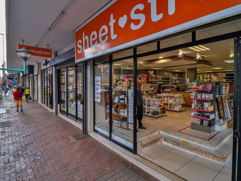 Commercial storefront featuring a glass facade, prominent signage, and a tiled entrance step located on a brick-paved street.