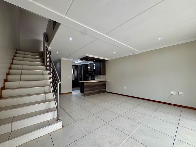 Open plan living area featuring a tiled staircase with stainless steel balustrade and a modern kitchen with dark cabinetry and island.