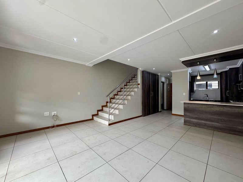 Spacious open-plan living area featuring large floor tiles, a modern staircase with stainless steel railings, and a sleek kitchen with built-in cabinetry.
