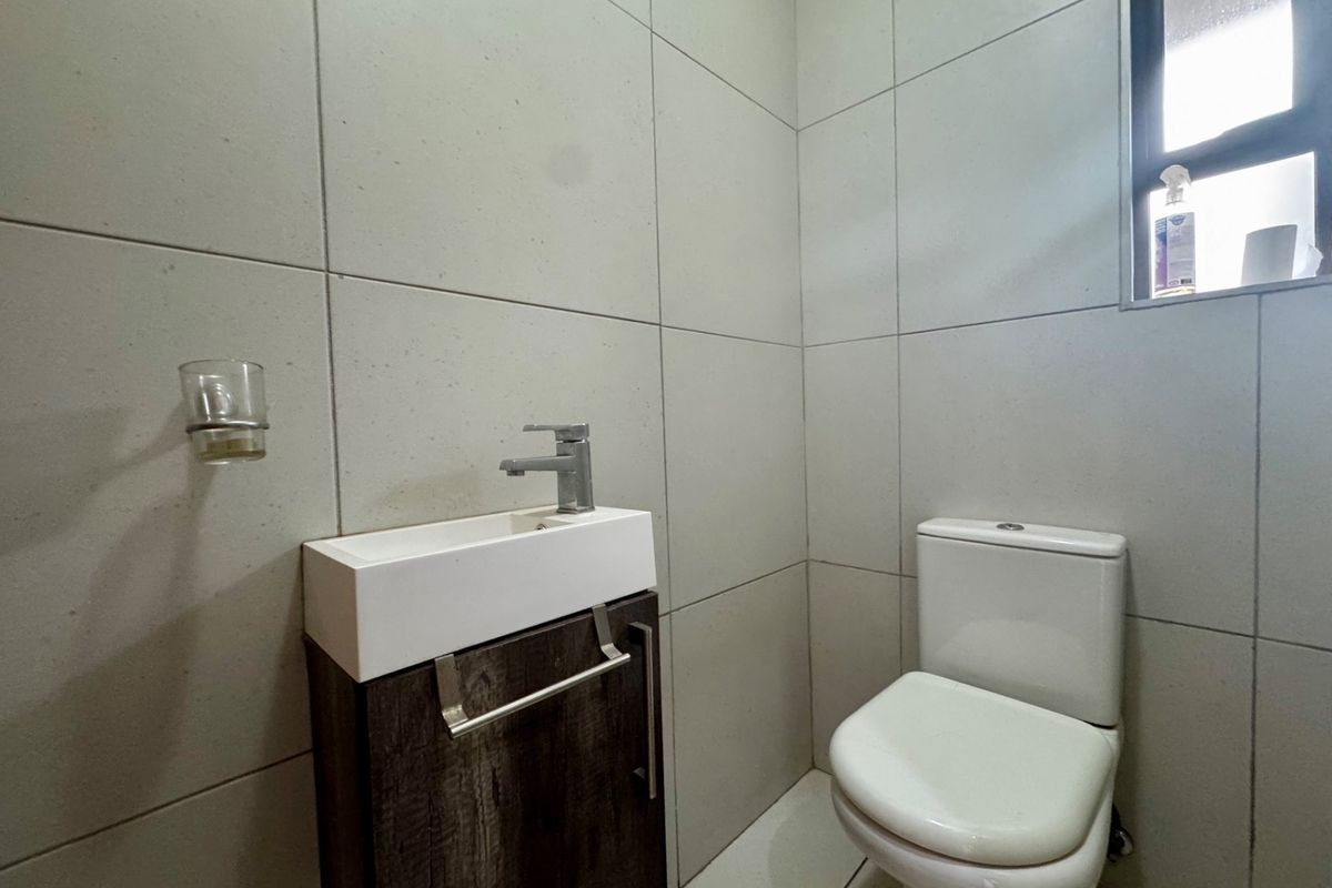 A compact, modern guest bathroom featuring floor-to-ceiling tiling, a wall-mounted vanity with basin, and a standard toilet.