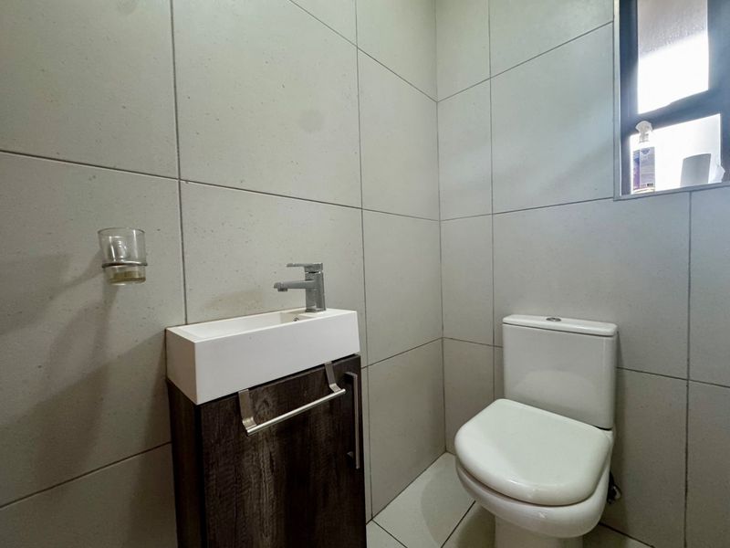 A compact, modern guest bathroom featuring floor-to-ceiling tiling, a wall-mounted vanity with basin, and a standard toilet.