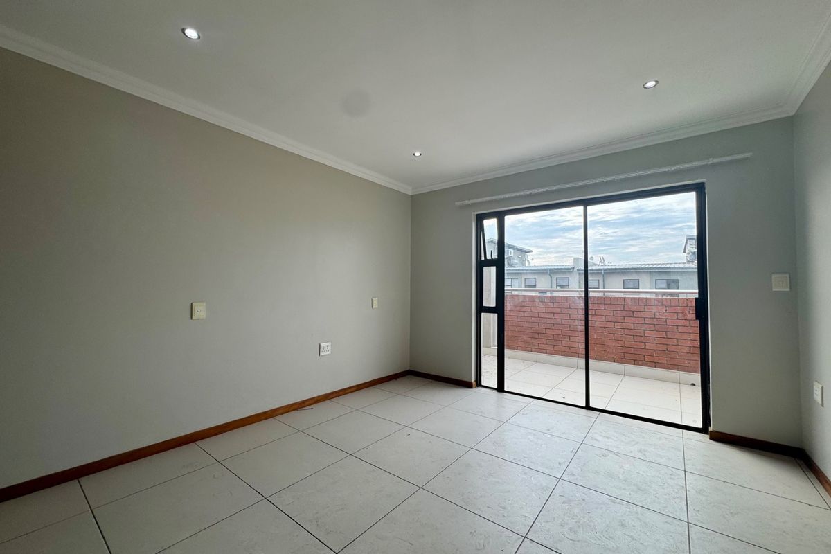 A bright, empty bedroom featuring neutral tiled flooring, recessed downlighting, and a sliding glass door providing access to a private balcony.