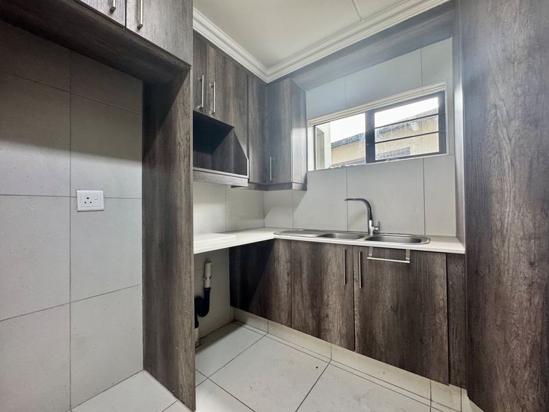A clean and functional scullery featuring modern wood-look cabinetry, a double bowl sink, and tiled finishes with dedicated plumbing for appliances.