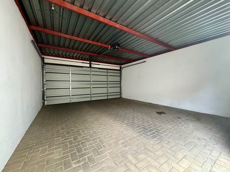 A clean, empty garage featuring a sectional door, paved flooring, and an exposed steel roof structure.