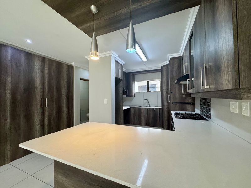 Modern kitchen featuring dark wood-grain cabinetry, stone countertops, a gas hob, and integrated lighting, offering a clean and functional workspace.