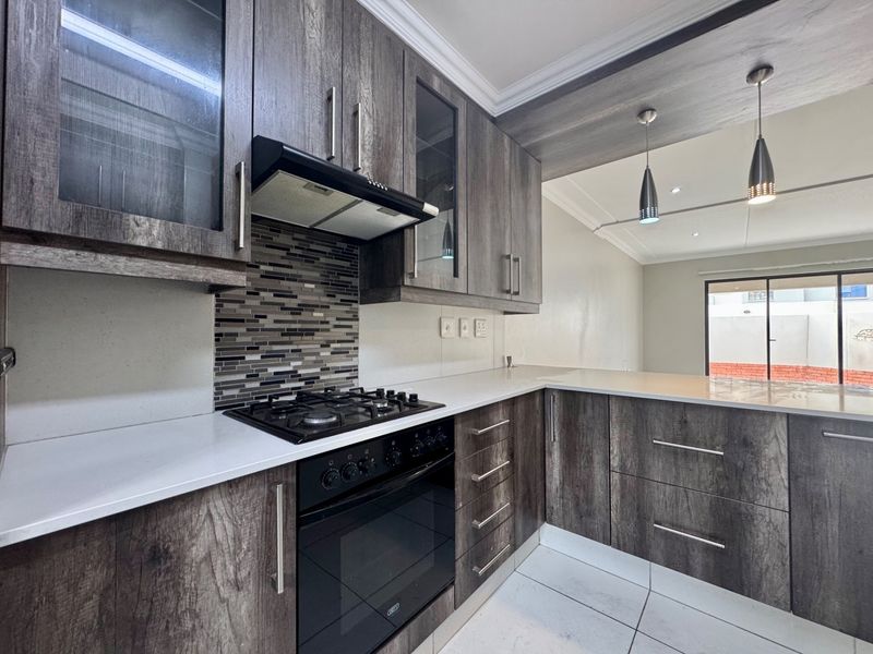 Modern kitchen featuring dark wood-grain cabinetry, stone countertops, a gas hob with extractor fan, and a stylish mosaic tile backsplash.